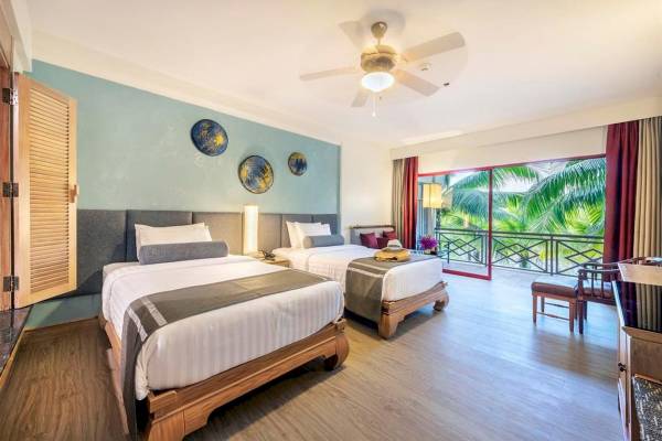Doppelbett-Zimmer im Chada Thai Village Resort mit Balkon und Blick auf Palmen.