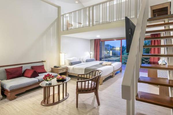 Ein modernes Hotelzimmer im Chade Thai Village Resort mit einem Doppelbett, einem Sofa, einem Tisch und einem Fernseher.