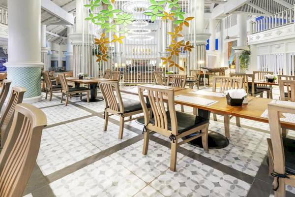 Innenbereich des Chada Thai Village Resort Restaurants mit Holztischen und Stühlen, weißer Wandgestaltung und Blattdekoration.