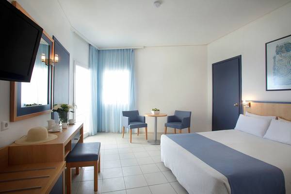 Ein modernes Hotelzimmer mit blauen Vorhängen und weißen Böden, einem Bett mit blauen und weißen Laken, einem kleinen Tisch und zwei Stühlen.