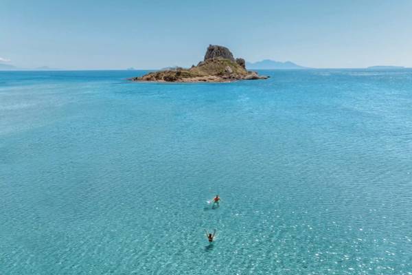 Zwei Leute schwimmen im klaren Wasser vor einer kleinen Insel.