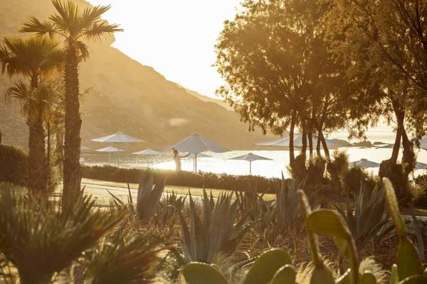 Sonnenaufgang im Ikos Aria Hotel mit vielen weißen Sonnenschirmen und einem Berg im Hintergrund.