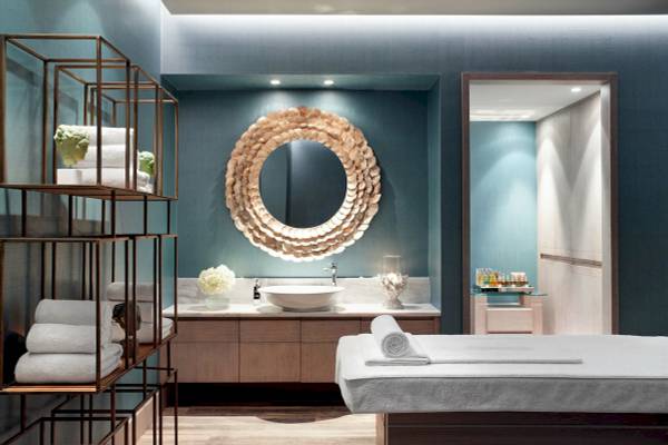Wellnessbereich im Ikos Aria Hotel mit runden Spiegel, weißen Handtüchern und einer Tischlampe.