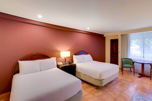 Doppelzimmer im DoubleTree by Hilton Hotel Cariari San Jose mit zwei Betten, Tisch, Stühlen und Fenstern.