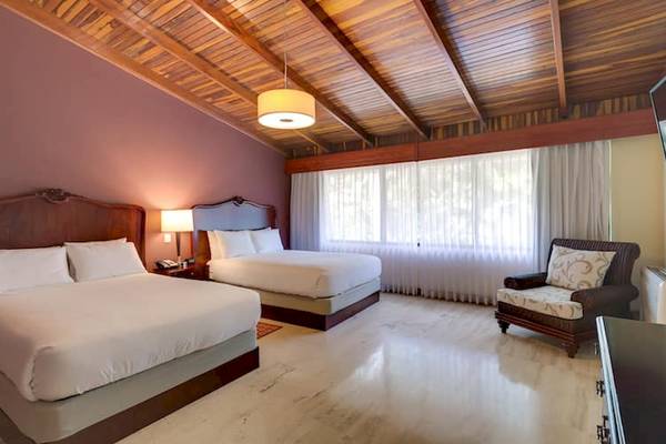 Doppelbett-Zimmer im DoubleTree by Hilton Hotel Cariari San Jose mit zwei Betten, Lampe, Fenstervorhängen und einem Sessel.
