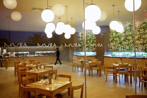 Innenansicht des Restaurants im Mura Mura Hotel mit Holztischen, Stühlen und großen Glaslampen.