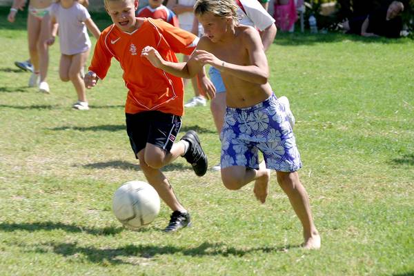 Kinder spielen Fussball auf einer Rasenflaeche, einer juengt verfolgt den Ball.