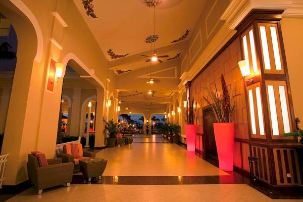 Innenansicht des Foyers des Riu Guanacaste Hotels mit langen Flur, Sesseln, Pflanzen und leuchtenden Laternen.