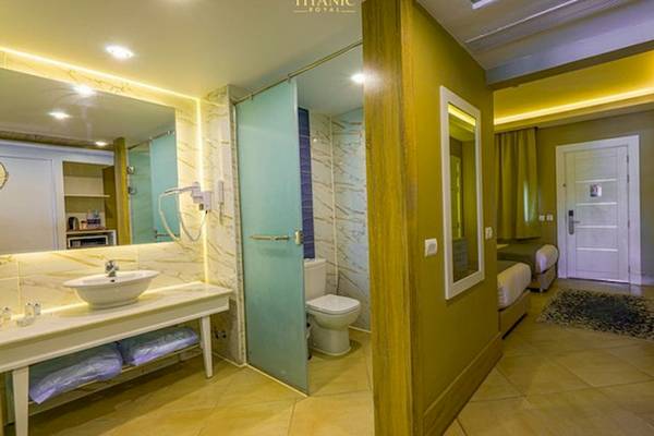 Ein modernes Badezimmer im Titanic Royal Hotel mit einer Dusche, Toilette, Waschbecken und einem Bett.
