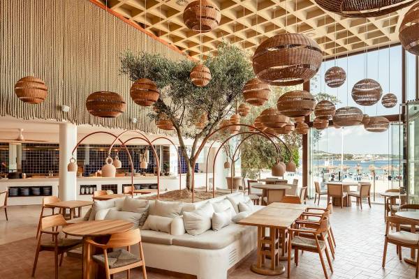 Inneneinrichtung des Zel Mallorca Hotels mit modernem Design, großen Couch, Holztischen und Stühlen und Blick auf den Strand.