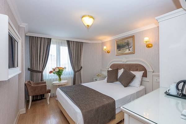 Ein elegantes Schlafzimmer im Arden City Hotel mit einem Doppelbett, einem kleinen Tisch mit Blumen und einem Sessel.