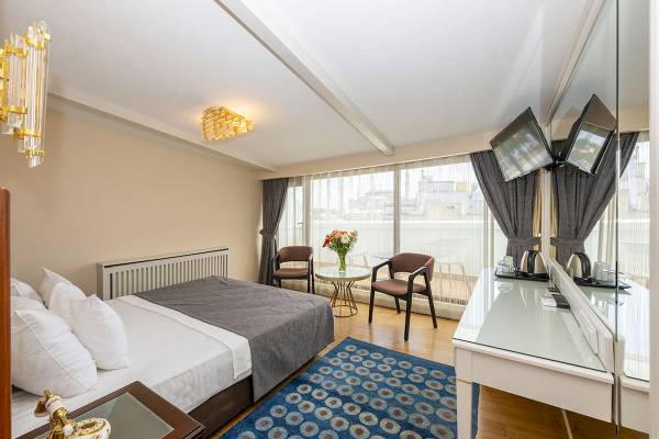 Innenansicht eines Hotelzimmers im Arden City Hotel mit Bett, Stühlen, Schreibtisch und Fenstern.