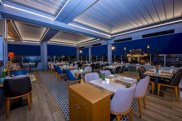 Nachtansicht der Dachterrasse des Arden City Hotels mit beleuchteten Tischen und Stühlen.