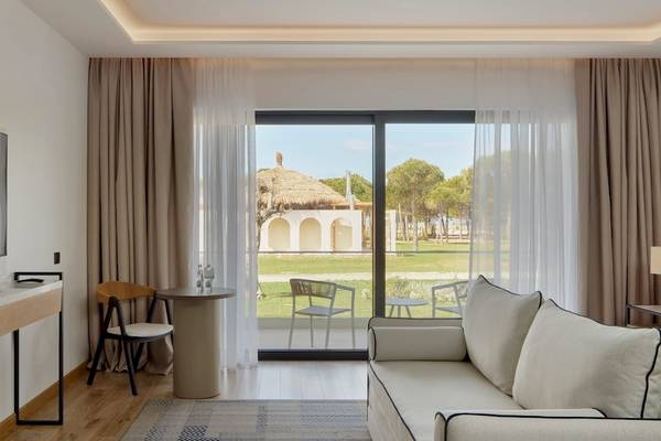Innenansicht eines Hotelzimmers im Melia Durres Albania mit einem großen Fenster, das auf eine Terrasse und eine Rasenfläche führt.