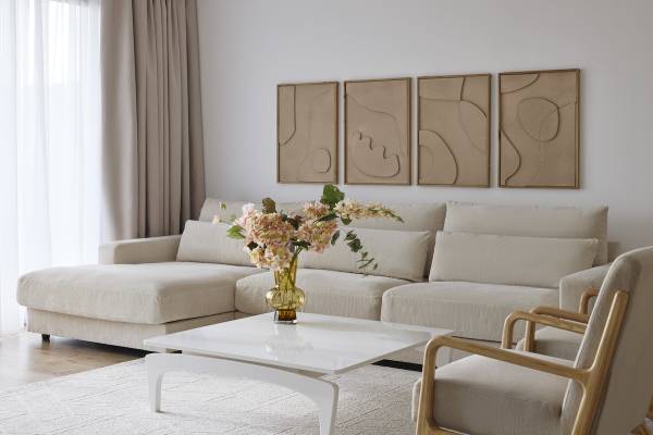 Wohnzimmer im Melia Durres Hotel in Albanien mit beigefarbener Couch, Blumenvase und drei Wandbildern.