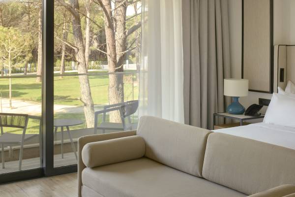 Sofa im Melia Durres Albania Hotel Zimmer mit Blick auf eine Terrasse und Bäume.