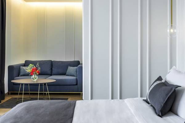 Suite-Zimmer im Mövenpick Hotel Lalez Durres mit heller Einrichtung, grauem Bett und Sofa, runden Tisch mit Blumenvase.