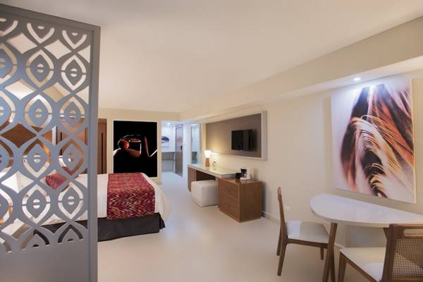 Innenansicht eines Hotelzimmers im Emotions By Hodelpa Puerto Plata, mit Bett, Schreibtisch und Kunstwerk.