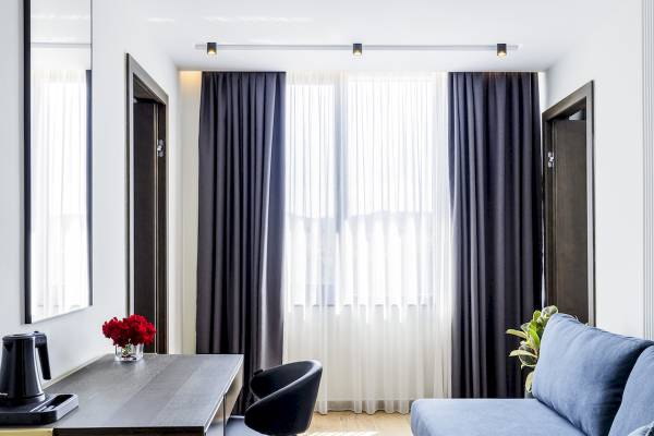Innenansicht eines Zimmers im Mövenpick Hotel Lalez Durres mit Schreibtisch, Stuhl, Sofa und Fenstervorhängen.
