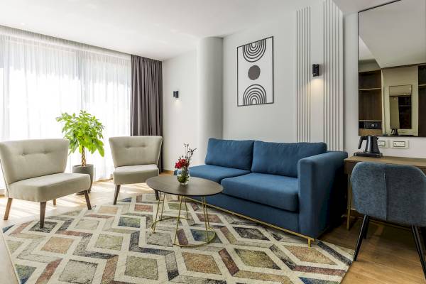 Wohnzimmer im Mövenpick Hotel Lalez Durres mit blauem Sofa, Teppich und Dekopflanzen.