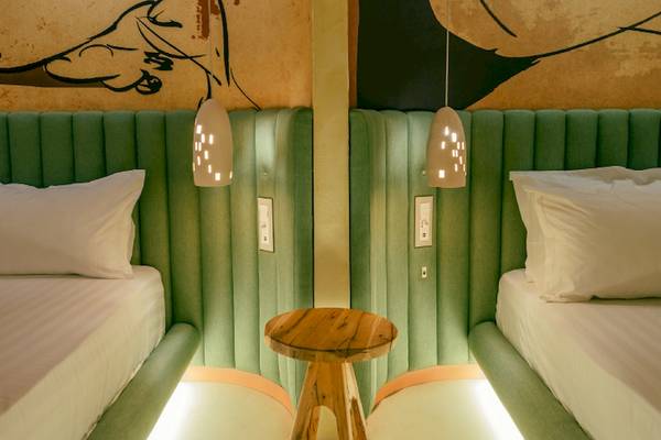 Doppelbettzimmer im Epidamn White Sensation Hotel mit grünen Kopfteilen, weißen Laken und Kissen, und einem kleinen Holztisch dazwischen.