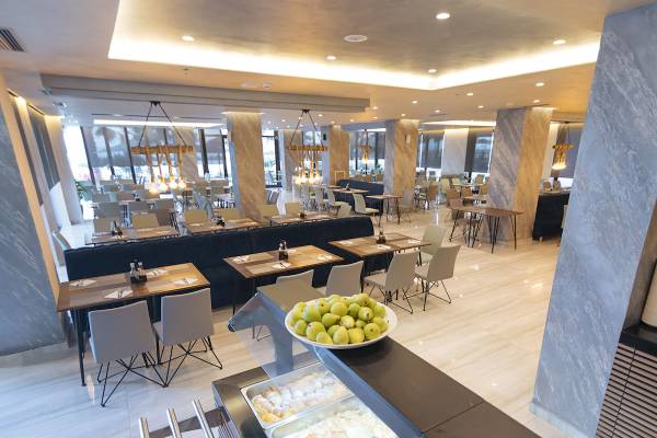Innenansicht des Restaurants im Brilliant Hotel & Spa mit runden Tischen und Stühlen, einer langen Theke und einer Schale mit grünen Früchten.