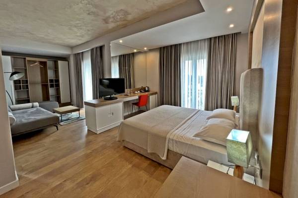 Innenansicht eines modernen Hotelzimmers mit einem großen Bett, Fernseher, Schreibtisch und Fenstern.