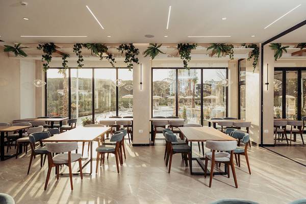 Innenansicht des Speisesaals des Delight Hotels mit großen Fenstern und grünen Pflanzen