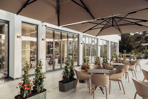 Terrasse des Delight Hotels mit Tischen, Stühlen und Pflanzen unter Sonnenschirmen.