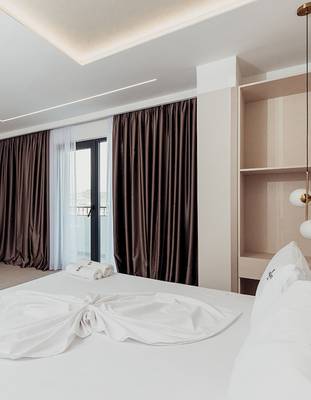 Schlafzimmer im Delight Hotel mit weißem Bett und braunen Vorhängen.