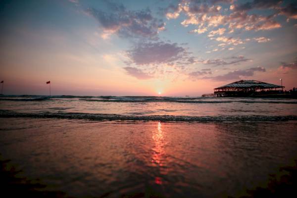 Sonnenuntergang am Strand mit einem Pavillon im Hintergrund und roten Fahnen im Wasser