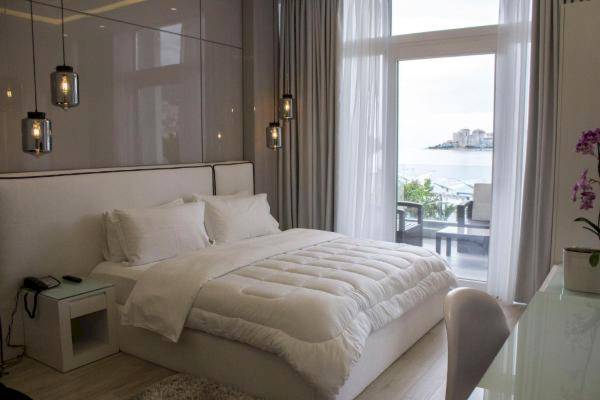 Schlafzimmer mit Meerblick im Demi Hotel mit großem Bett, weißen Vorhängen und Balkon.