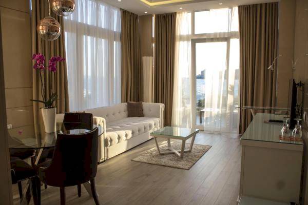 Wohnzimmer des Demi Hotels mit weißem Sofa, Glastisch und Blick auf die Stadt.