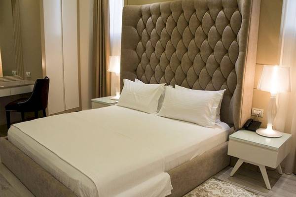 Schlafzimmer im Demi Hotel mit einem großen Bett, weißem Laken, zwei Kissen und einer gepolsterten Kopfstütze.
