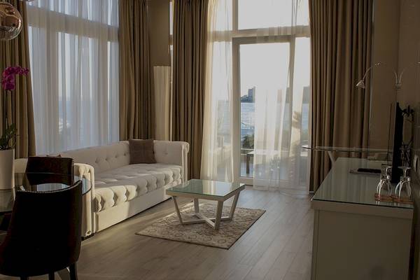 Ein Hotelzimmer mit einem weißen Sofa, einem Glastisch, einem Strauß violetter Orchideen und großen Fenstern mit Blick auf das Meer.