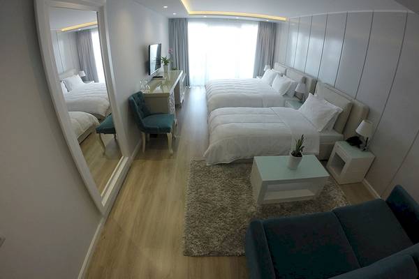 Schlafzimmer im Demi Hotel mit drei Doppelbetten, Couch, Tisch und Fernseher.