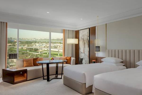 Suite-Zimmer im Grand Hyatt Dubai mit zwei Betten, Tisch, Sofa und Stadtblick.
