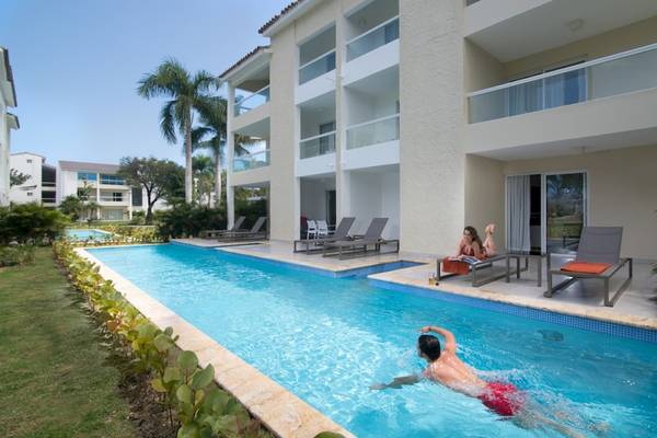 Mann im Swimmingpool des Emotions By Hodelpa Hotels, während eine Frau auf der Sonnenliege liest.