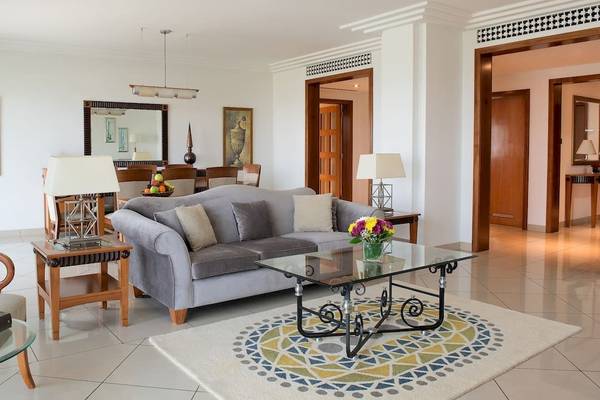 Wohnzimmer des Grand Hyatt Dubai mit grauem Sofa, Glastisch, Blumenvase und zwei Lampen.