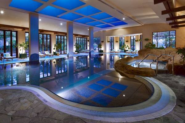 Innenpool im Grand Hyatt Dubai mit blauer Beleuchtung und umgeben von Lounge-Möbeln.