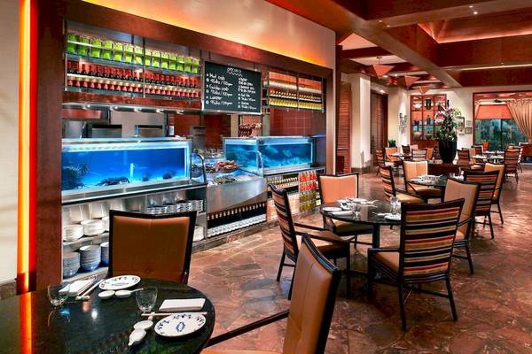 Innenraum des Grand Hyatt Dubai Restaurants mit Tischen, Stühlen, Meeresfrüchte-Aquarium und Pflanzen.