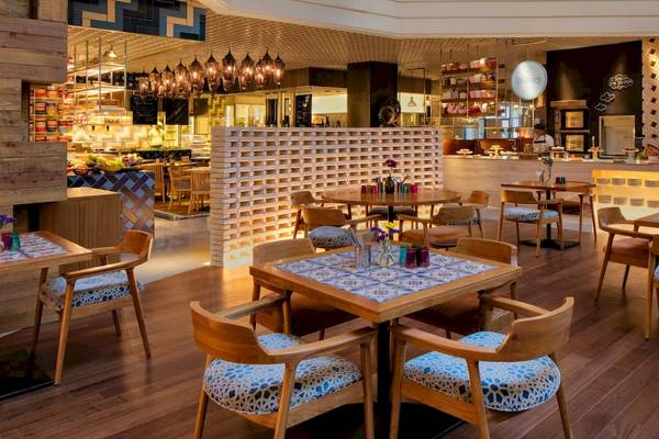 Innenansicht des Restaurants im Grand Hyatt Dubai mit Holztischen und Stühlen, dekorativen Wänden und Beleuchtung.
