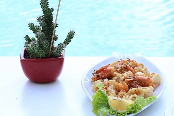 Nahaufnahme eines gegrillten Garnelen- und Tintenfischtellers mit Salat und Zitrone auf einem Tisch neben dem Dyrrah Hotel Pool