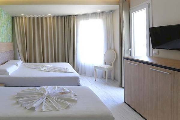Schlafzimmer im Dyrrah Hotel mit zwei weißen Betten, flauschigen Kissen und tropischen Wandmustern.