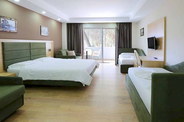 Zwei Zimmer im Dyrrah Hotel mit Doppelbetten und Sofas neben einem Balkon.
