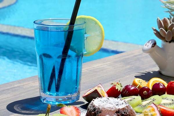 Dyrrah Hotel Poolseite mit einem Glas blauem Getränk, einer Zitronenscheibe, einer Obstplatte und einem Topf mit Sukkulenten neben dem Pool.