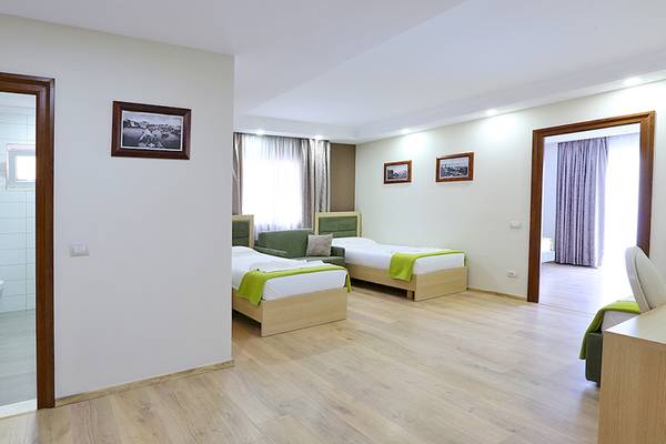 Schlafzimmer im Dyrrah Hotel mit zwei Betten, grünen Kissen und einem Sofa.