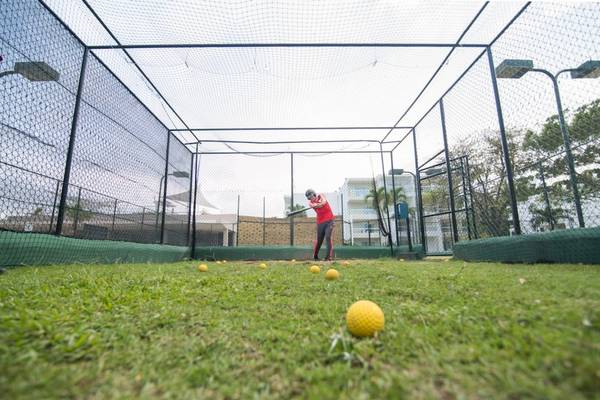 Golftraining unter einem Netz auf einem gepflegten Rasen.