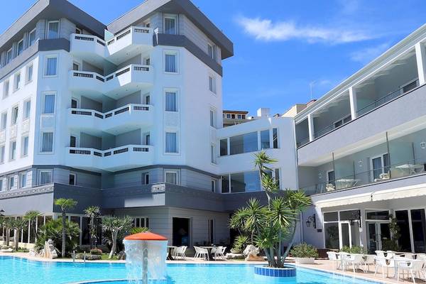 Außenansicht des Dyrrah Hotels mit Swimmingpool, weißen Sonnenliegen und grünen Palmen