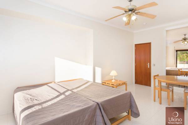 Innenansicht eines Schlafzimmers im Ukino Terrace Algarve Hotel mit zwei Betten, Nachttisch, Lampe, Esstisch und Stühlen.
